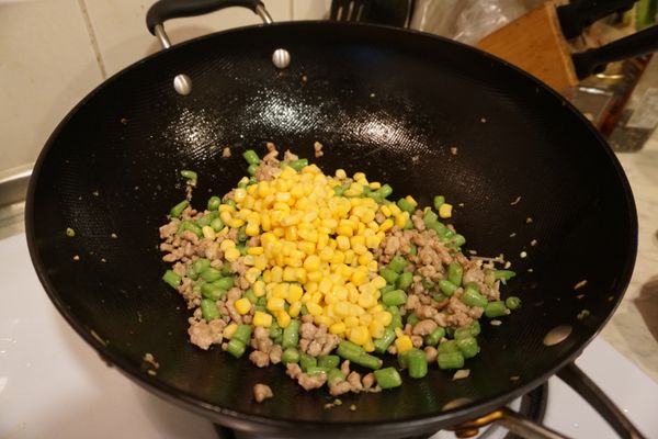 起鍋將肉末炒香，加入蒜末後拌炒，再放入四季豆炒，四季豆一定要炒熟(也可以將四季豆先川燙一遍，再加進來炒，可縮短拌炒時間)，最後放入黃米粒，因為是罐裝玉米粒，已經是熟的，所以玉米粒炒一下加熱，最後加入調味料即可。