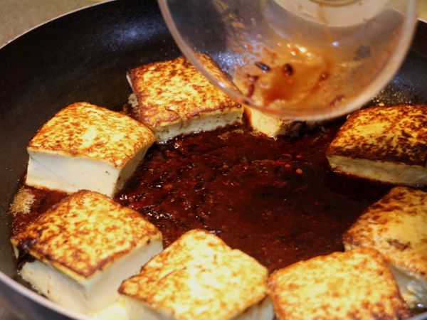 待豆腐兩面微焦時撥至鍋邊，中間倒入步驟2的醬汁，略微燒滾後加入毛豆仁和冷水，蓋上鍋蓋，以小火燜燒約5分鐘。