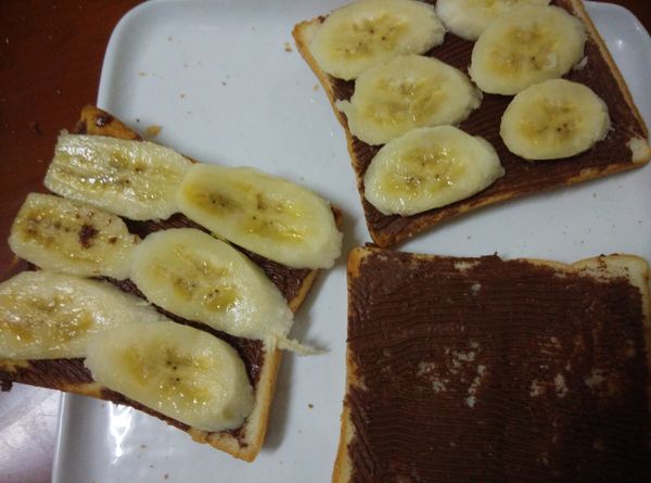 將香蕉片平舖在抹了巧克力醬的土司上。