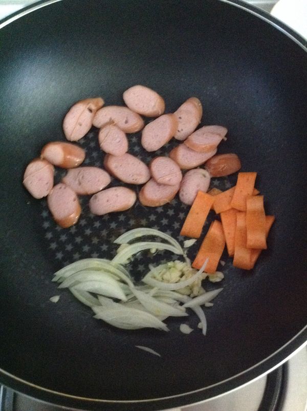 不粘鍋倒入少許橄欖油，鍋的一邊爆香洋蔥蒜米，一邊煎香腸，一邊爆香紅蘿蔔。