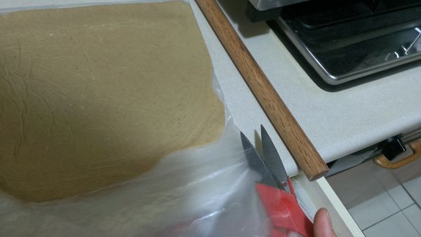 將麵糰取出後，桿成0.3-0.5公分厚的薄片，使用剪刀把外面大袋剪開，準備壓型