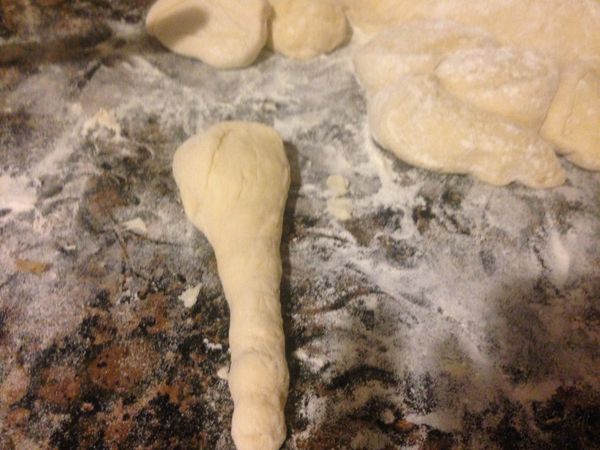 工作台上撒一些麵粉，將發好的麵團倒出來，上面再撒些手粉，麵包的麵團有些濕黏，這個很正常。手粉的作用就是防沾，揉圓麵團以後對切，再將兩個半圓型麵團揉成兩條，各切10個小麵團，拿起一個麵團，撒手粉，雙手一起搓，搓出一個水滴型如圖。