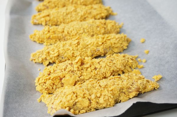 將醃漬好的雞里肌肉依序沾上低筋麵粉、蛋液、玉米脆片，壓緊後放在鋪了烘培紙的烤盤上。