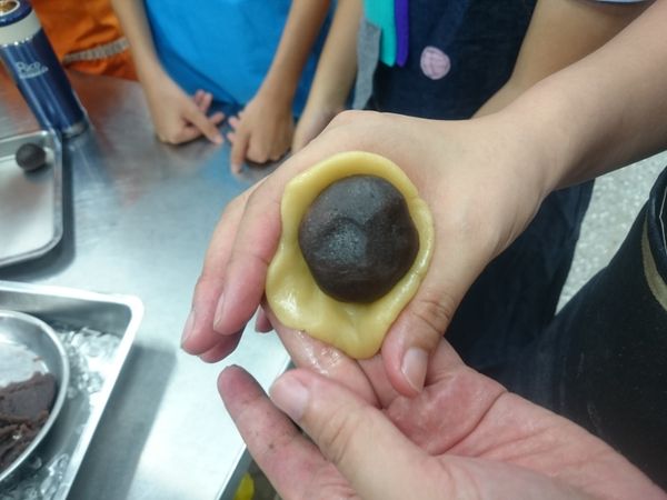 拿起一個豆沙球，用手指在中央開一洞，把半個鹹蛋黃包在豆沙裏面，滾圓後，放在麵團皮中央，小心包起來