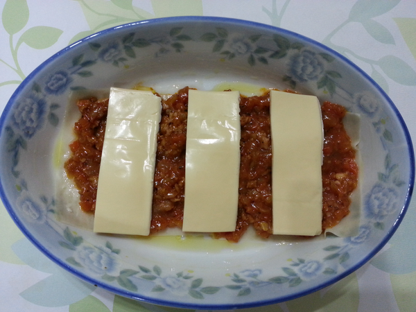 在餛飩皮上鋪一層茄汁肉醬,肉醬上面再鋪一層起司片.依序再重複做二次