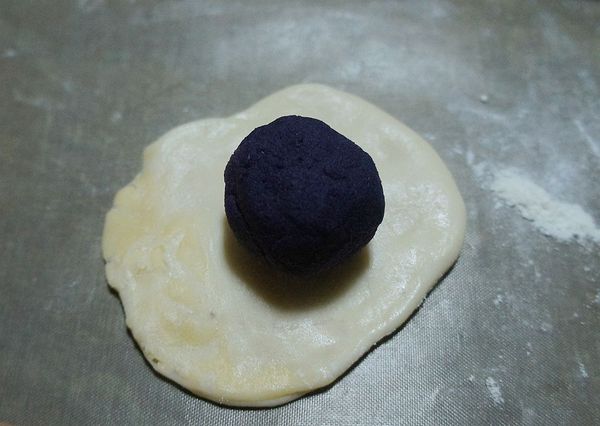 包入滾圓的紫薯餡包緊，收口朝下用擀麵棍撖呈橢圓扁狀，中心切一刀用預熱至180度烤箱烤20~25分鐘表面金黃即可。