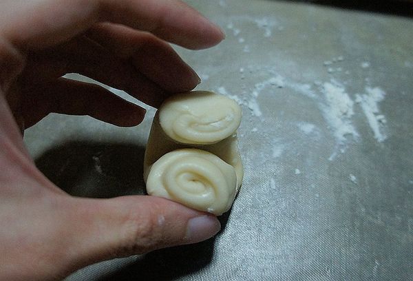 將鬆弛好的長型水油皮油酥條直放上下抓起往下壓扁成外薄中心厚的圓形麵皮。