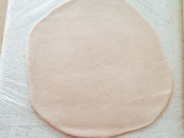 用擀麵棍擀成一片長方型之後撒點水，將麵皮由長向密實捲起，收口朝下