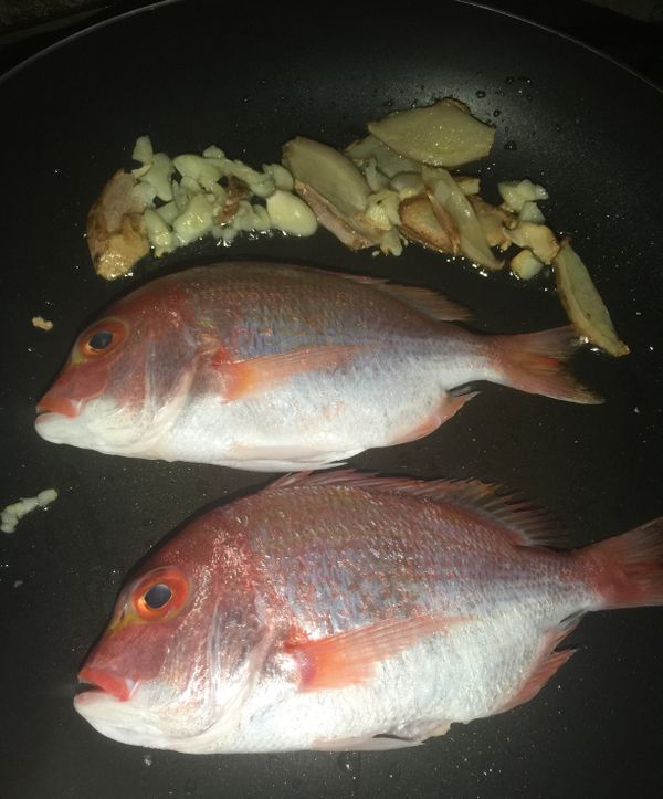 然後把爆過的蒜粒及薑片放在鍋邊，然後由爆香的油把魚放入鍋中乾煎至熟。