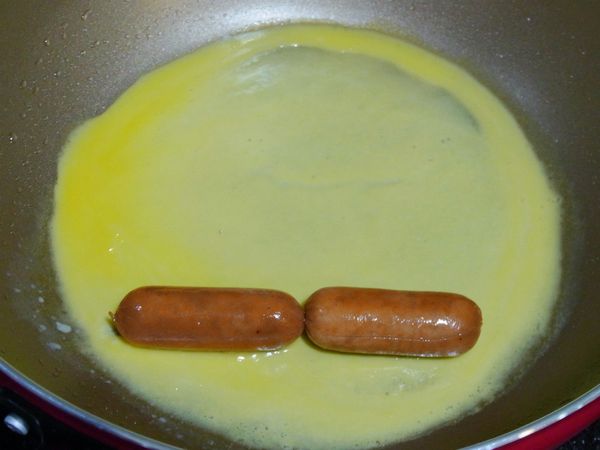 〈玉子燒瓢蟲的做法〉蛋加鹽調味拌勻，鍋子抹一層油煎，放上熟的小熱狗捲起來，