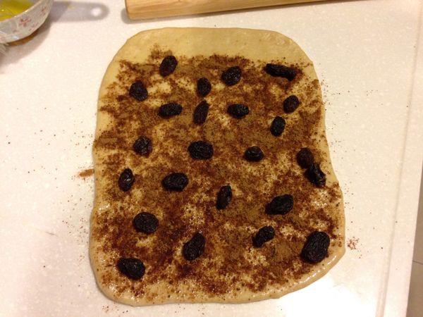 桿成長方狀，刷上溶化的奶油，留一側2~3公分不用刷， 糖+肉桂混合後，均勻的灑在刷了奶油的麵團上，再灑上適量 葡萄乾，一樣留一側2~3公分不用灑