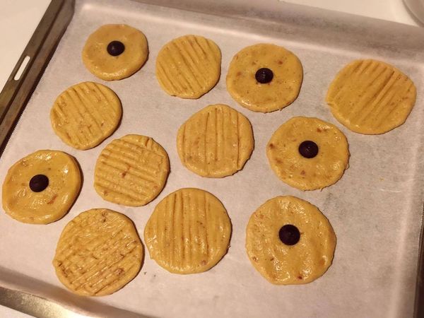 將餅乾麵糰用手搓成大小相等的圓型狀，排放在舖有烘焙紙的烤盤上，再用手掌輕輕壓扁成餅乾狀，中間可以放上巧克力豆當裝飾，也可以用叉子劃上紋路