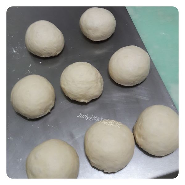 將第一次發酵好的麵團移出到桌面，麵團中的空氣用手壓下去擠出來，分割成8個麵團，分別滾圓，蓋上保鮮膜休息15分鐘