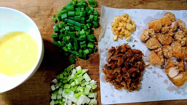 準備配料：將蒜味鹽酥雞的蒜頭和鹽酥雞分開，鹽酥雞切半，雞皮切碎、蔥切成蔥花（葱白和葱綠分開）、蛋打成蛋液備用。