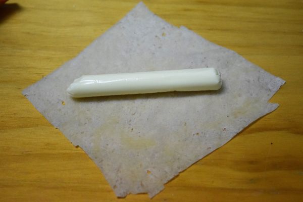 春捲皮對折，剪成兩個方形，取一張，包起一條起司條