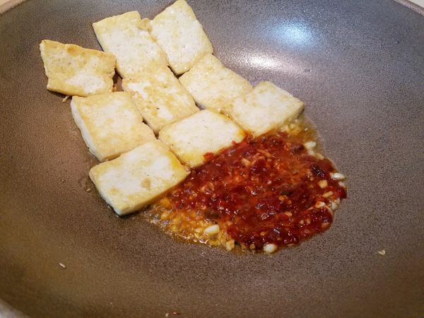 將豆腐推到一邊，爆香蒜薑末及辣豆瓣醬，再將豆腐一同拌炒。