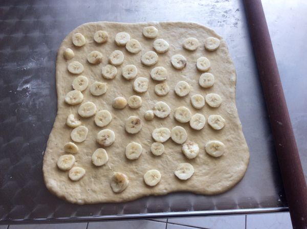 發酵完成的麵團壓出空氣後擀成方形麵片。兩根香蕉切薄片舖上。