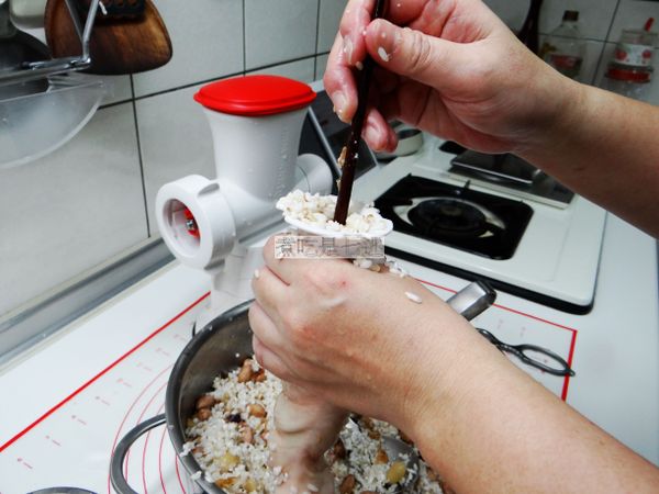 拿一個漏斗(只要花生掉的下去的，就可以用)，用湯匙裝適量的米餡料，倒進漏斗，再用一根筷子(粗的那頭)戳進去大腸裡面，再用手將餡料往下推