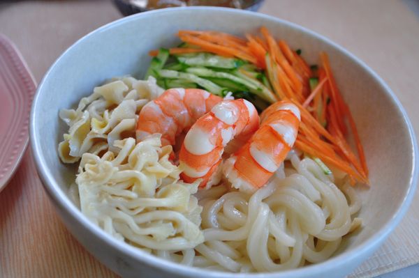 將冰鎮的烏龍麵放入盆中，再擺入白蝦等配料