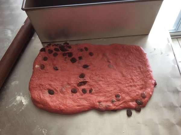 發酵完成後，紅色麵團揉進葡萄乾後擀成長方片，長度比吐司模略短一些。然後捲成長條。