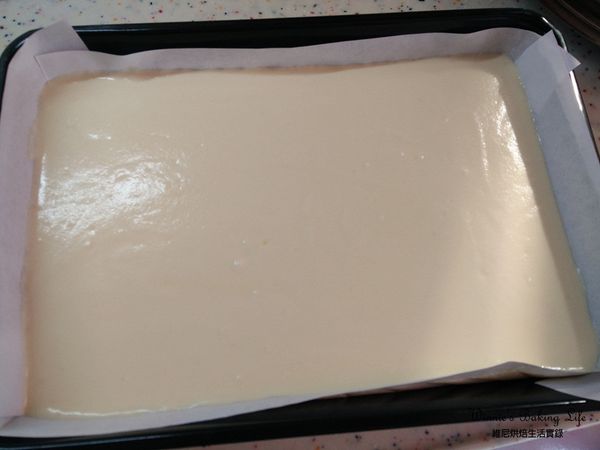 將混合好的蛋糕糊倒入鋪上白報紙的方型深烤盤中，在桌上重敲幾下，震出蛋糕糊內的大氣泡，讓表面平整一些