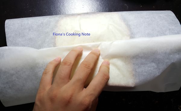 將蔬菜、肉、蛋夾進吐司。取一料理紙覆蓋吐司，收口處捲緊。