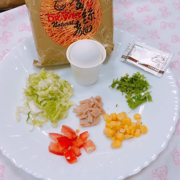 將金絲麵稍微捏碎,倒入碗裡,加入雞蛋、高麗菜、香菜、素火腿、番茄、玉米、麵糊,一包香菇粉調味,攪拌均勻