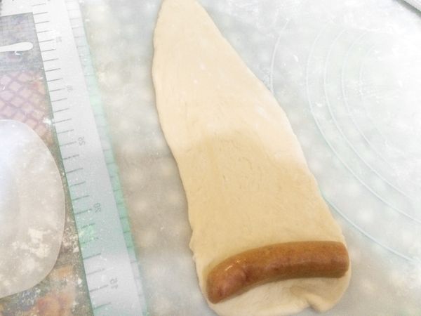 二次發酵完成後，取一麵糰桿平，翻面（把平整那一面向外，醜的那面朝內），把德式香腸切半，用桿平的麵團包住德式香腸，捲起