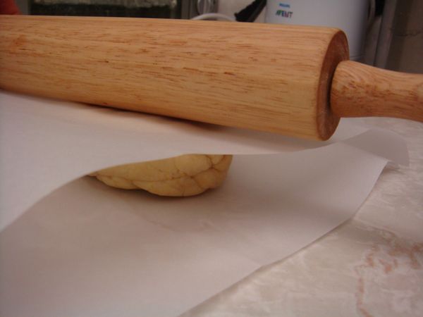 工作檯面鋪上防沾烤紙，取出並將麵糰放在烤紙上，麵團上方也鋪上一張防沾烤紙，就可開始將麵團擀開，約0.20公分厚 (太厚, 會膨脹的太高, 不美觀; 也不要太薄, 容易烤焦)