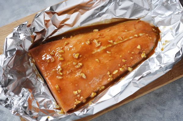 撕下一大張鋁箔紙，將鮭魚菲力放中間，在魚身倒1大匙白酒並抹勻，再淋上調好的醬汁，可保留1-2大匙，在上桌前使用。