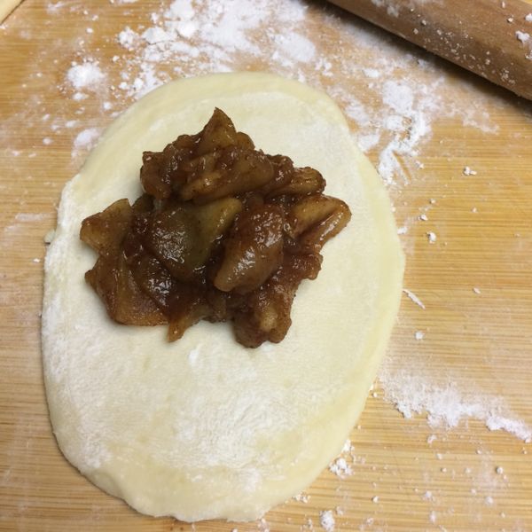 用蛋液刷橢圓派皮的邊緣，呈U字型。中間擺上冷卻的蘋果餡，將派皮對折封口。