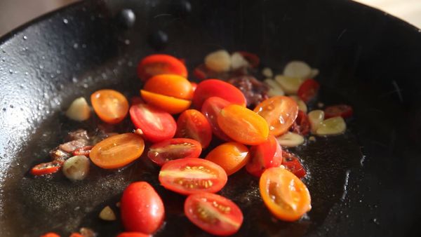 起油鍋，將大蒜、辣椒、鯷魚爆香後倒入小番茄拌炒。