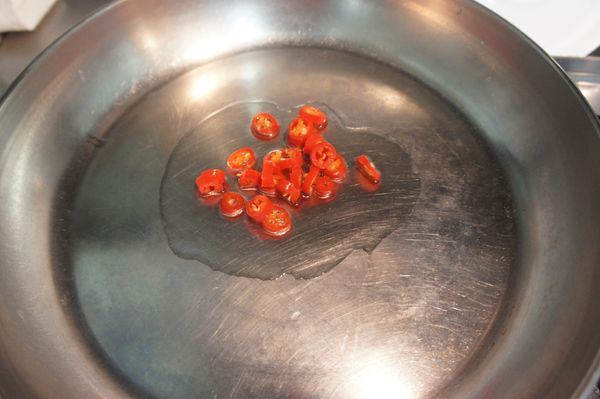 取平底鍋，加熱一大匙油後，放入紅辣椒丁炒出香氣。