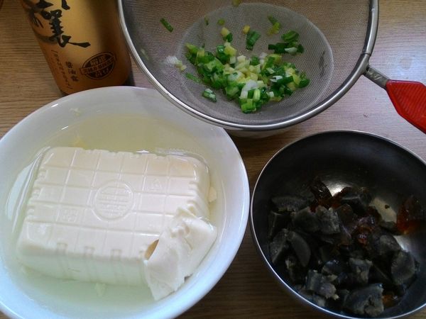 取出嫩豆腐將其放入碗中，另加冷開水泡著備用。利用此時將之前靜置放涼的皮蛋，剝殼後切成丁狀備用。