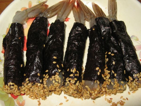 海苔片分成7-8等份，包裹蝦肉並捲起，露出前頭和尾部，前頭沾滿白芝麻。