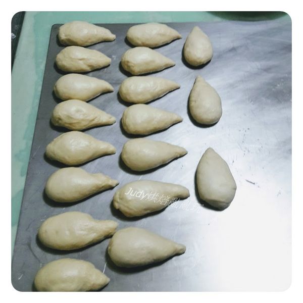 將第一次發酵好的麵團移出到桌面，麵團中的空氣用手壓下去擠出來，分割成18個麵團，分別滾成椎子狀，蓋上保鮮膜休息20分鐘