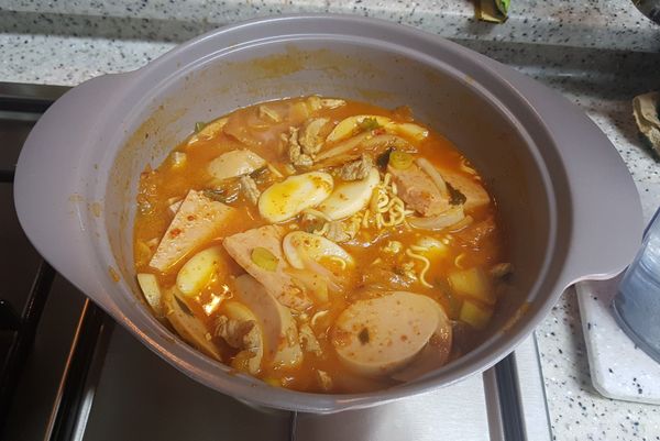 等高湯滾了後，將小魚乾及昆布撈乾淨，再將豬肉、泡菜、洋蔥、蔥花、火腿、熱狗、年糕片及佐料都放入，待再次滾起來再下泡麵。