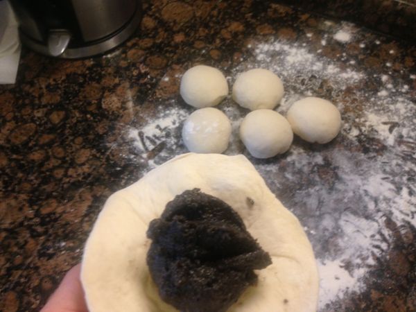 把每個麵團都揉成小圓麵團，桿麵的時候，接點朝上，用桿麵棍桿開麵團，包入芝麻餡兒，當然芝麻餡兒也由八份改成六份，接口捏緊朝下，光面朝上。然後放入蒸籠裡，當然下面要放防沾紙，一個一個做好放好。如圖。