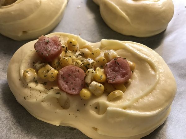 將玉米粒鋪在麵團上，放上切丁的小熱狗