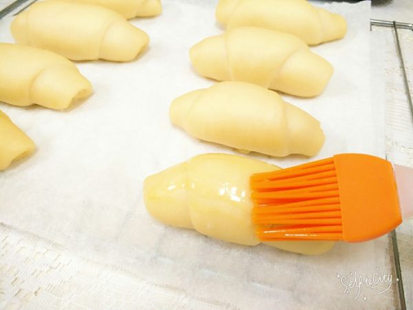 發酵完成前10分鐘，先將烤盤取出，烤箱預熱170度。將"塗表面用"的雞蛋打散，沾取蛋液，均勻塗抹在麵包捲的表面上