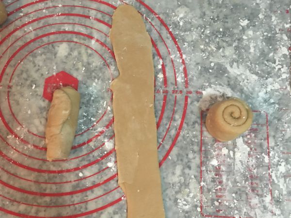 桌面和桿麵棍用麵粉抹一下，取一顆皮用手掌略壓後，用桿麵棍從中間上下輕桿成橄欖型後，用手指輕推捲起成長柱型。依續橄、捲好後；取第一個捲好的長柱型，開口朝上從中間輕桿成長條型，再捲起成短柱型，依續都要桿、捲成短柱型。