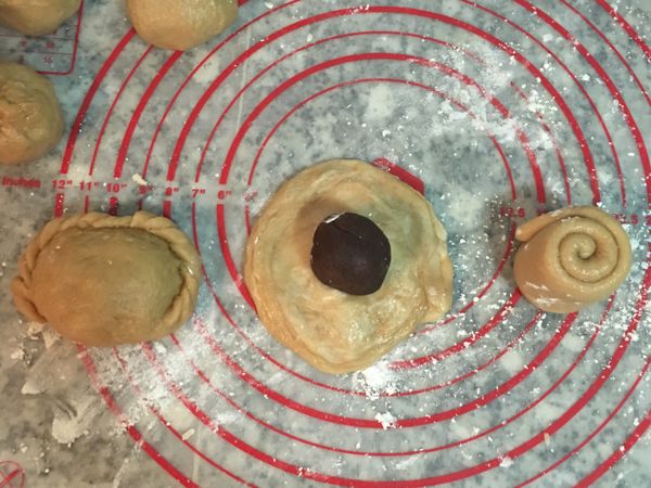 取第一個捲好的短柱型，用手掌壓扁後桿成中間後厚外圈薄的圓型，滾好後麵皮翻面，包入略壓扁的豆沙球，先包成半月型，開口都捏緊後再捏造型。