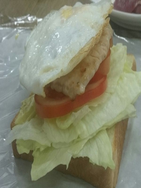 撕開一張保鮮模,約50公分長度,以一片吐司為底座,依序放上萵苣3片,雞蛋,番茄3片,里肌肉片,萵苣3片,最上層放上吐司一片,以保鮮模包裹全部食材起來。