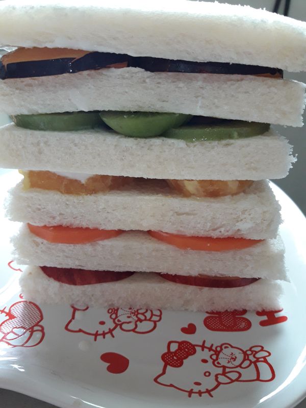 吐司兩邊都要塗優格哦，水果依顏色擺放，紅（蘋果）→橘（木瓜）→黃（柳丁）→綠（奇異果）→紫（黑李），這樣就完成囉~~~再拿鋸齒刀切開，就是美美的彩虹三明治囉~~~~~~