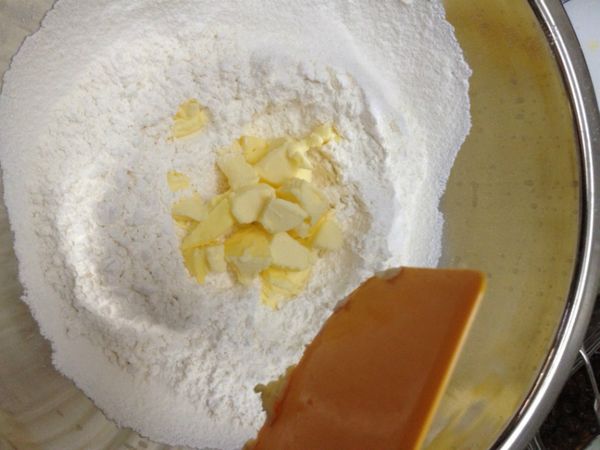 取出[乾料]，過篩兩次，加入糖、鹽拌勻，中間挖出一個凹槽到入奶油丁。